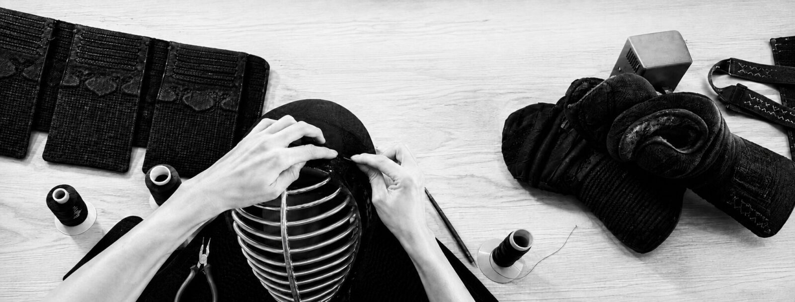 Black-and-white photograph of kendo equipment and hands working on a men at KOBUDO